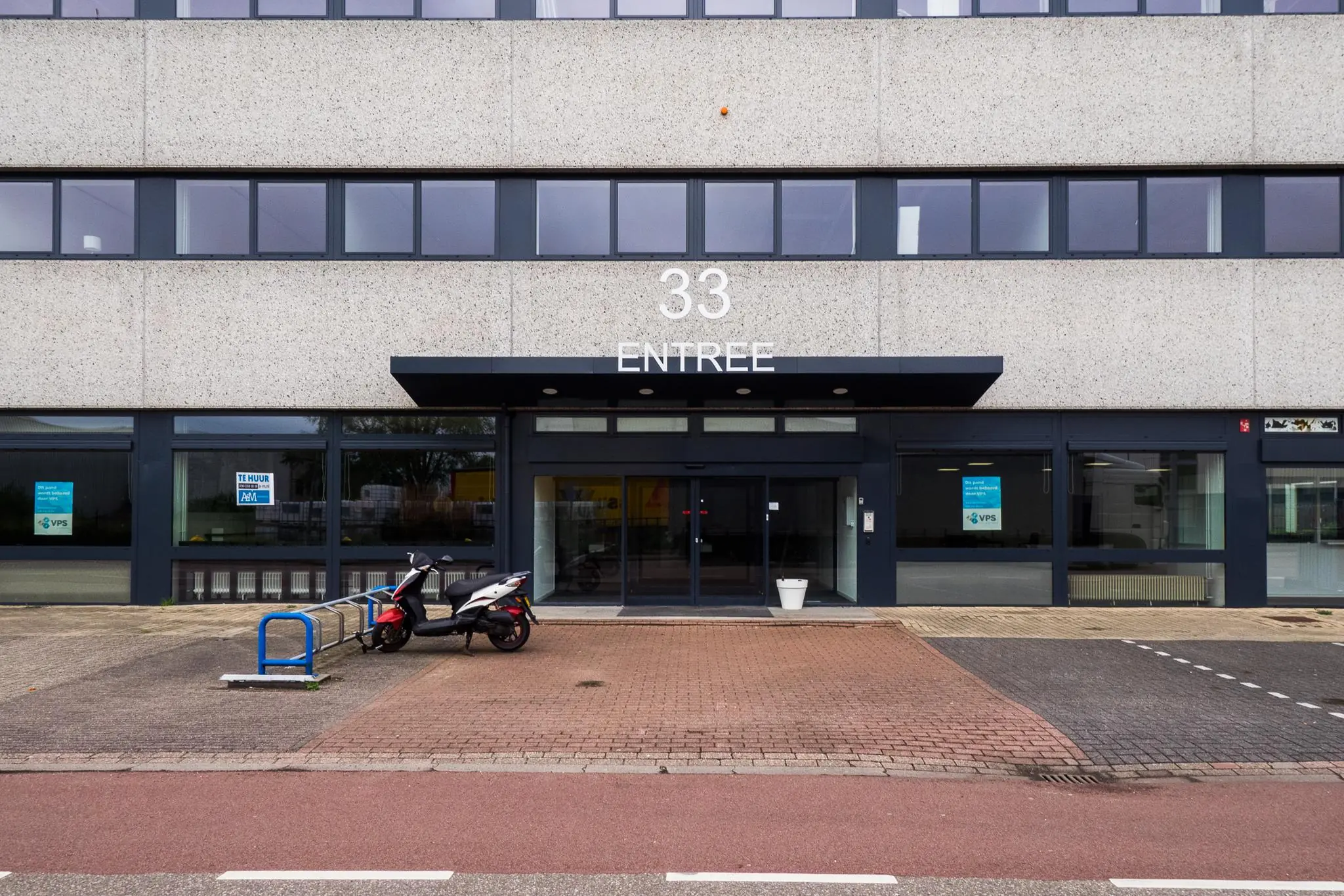Vooraanzicht van een kantoorpand aan de Zonnebaan 33 met een scooter geparkeerd bij de entree.