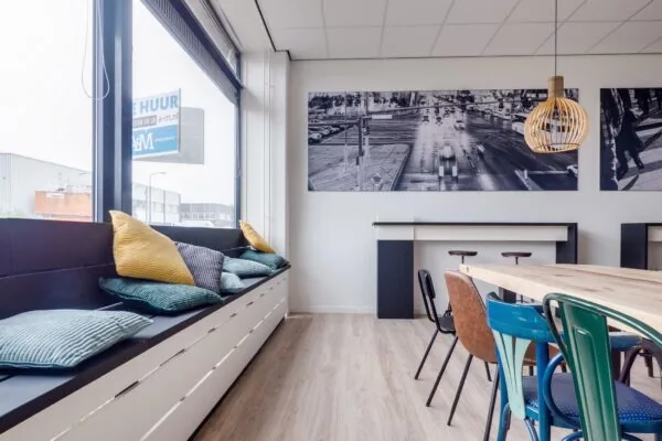 Moderne kantoorruimte aan de Zonnebaan met zithoek bij het raam, kleurrijke kussens, diverse stoelen en grote zwart-wit foto's aan de muur.