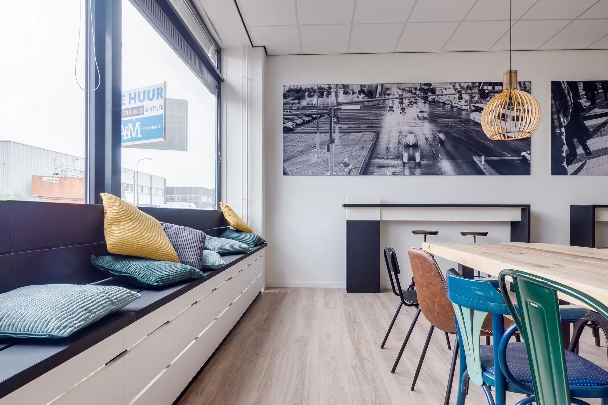 Moderne kantoorruimte aan de Zonnebaan met zithoek bij het raam, kleurrijke kussens, diverse stoelen en grote zwart-wit foto's aan de muur.