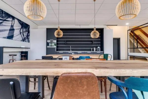 Moderne gemeenschappelijke keuken en zithoek met houten tafels, industriële stoelen en stijlvolle hanglampen in een kantoorruimte aan de Zonnebaan.