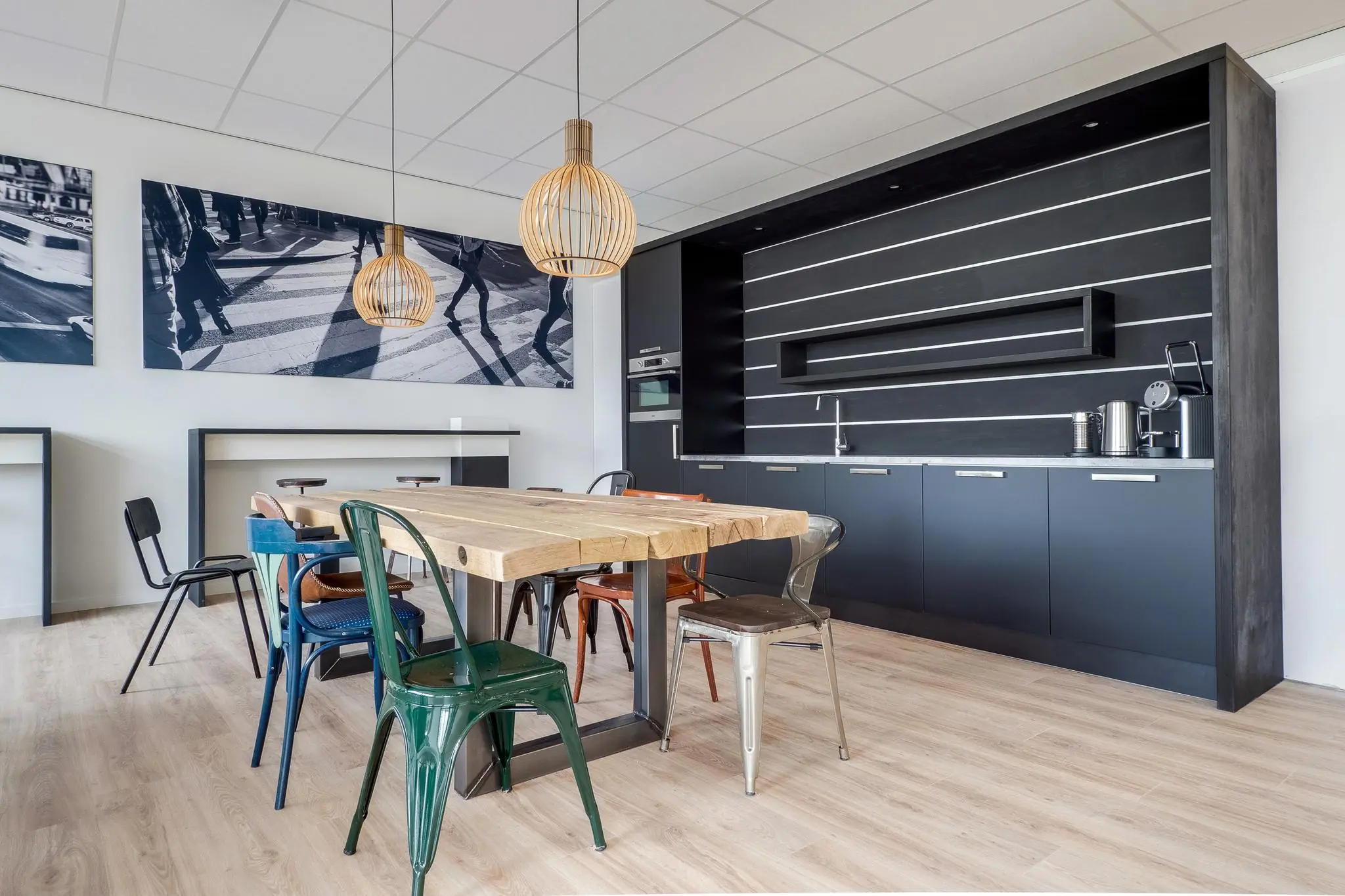 Moderne kantine met houten tafel, kleurrijke stoelen en een zwarte keukenwand in een kantoor aan de Zonnebaan.