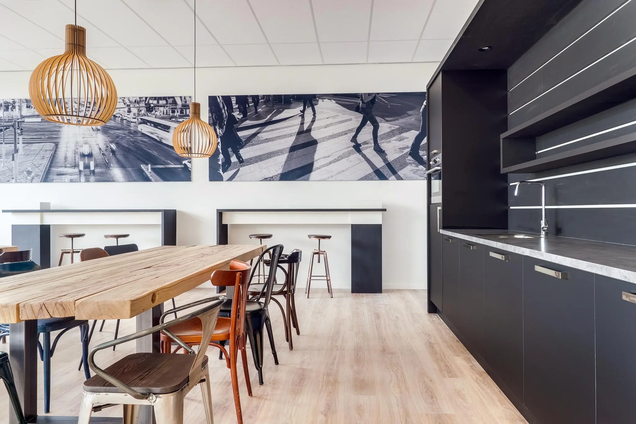 Moderne kantine met houten tafel, diverse stoelen, zwarte keuken en wanddecoratie van stadsfotografie.
