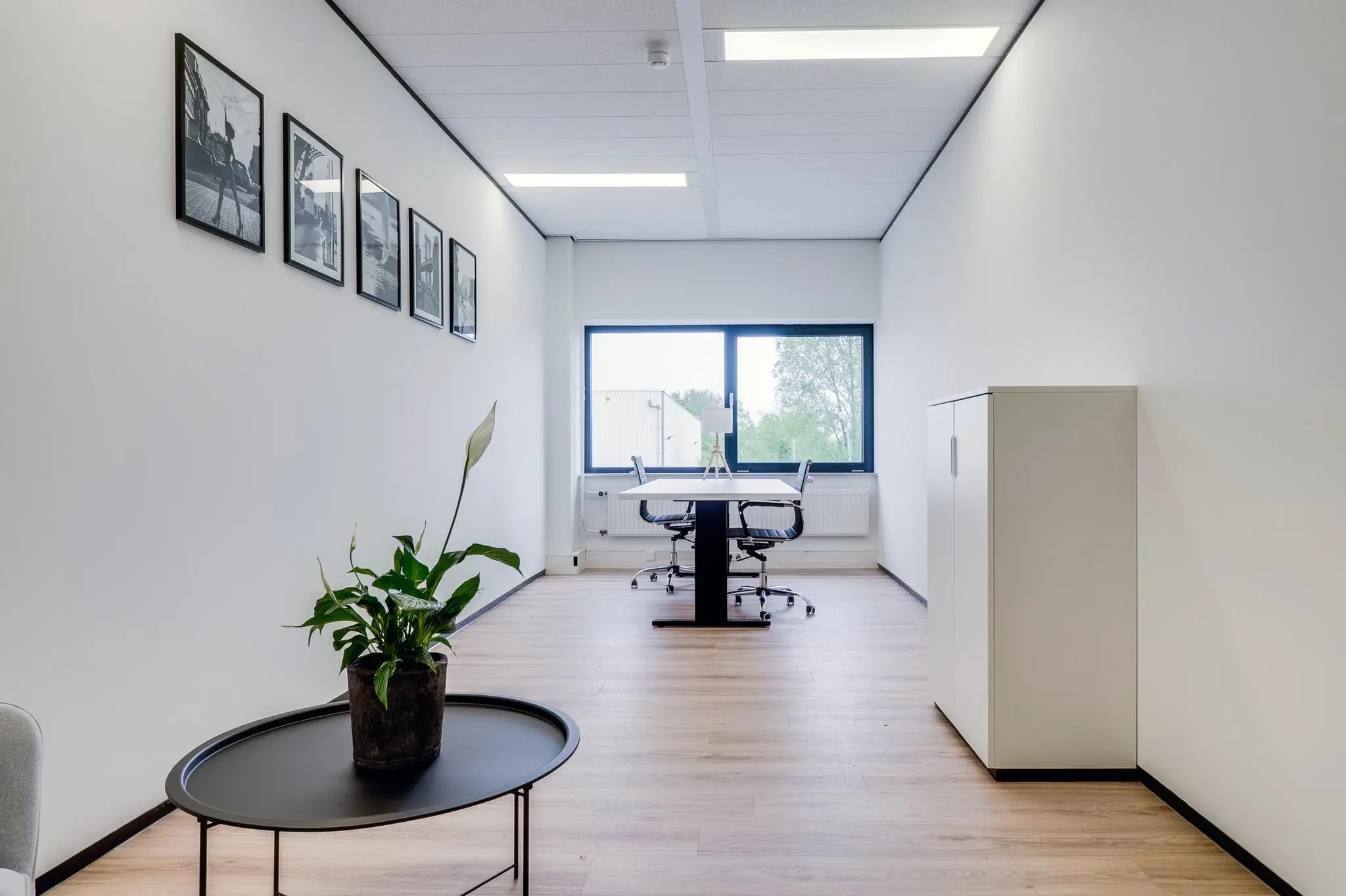 Modern ingericht kantoor aan de Zonnebaan met strakke witte muren, houten vloer, en een werktafel bij een groot raam.