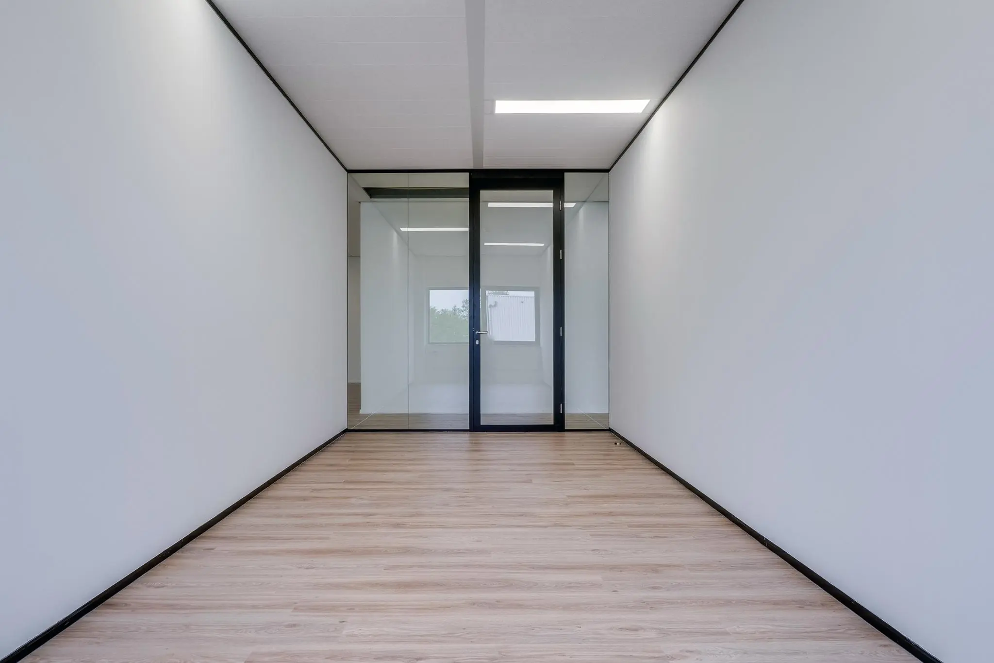 Lege, moderne kantoorruimte met laminaatvloer en glazen deur aan het einde.