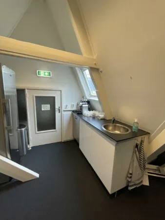 Kleine kitchenette in een zolderruimte aan de Raadhuisstraat met een aanrecht, wasbak en koffieapparaat.