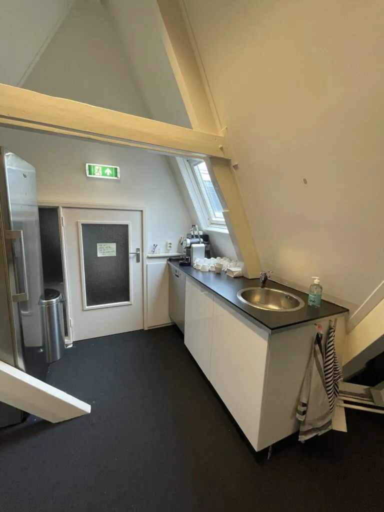 Kleine kitchenette in een zolderruimte aan de Raadhuisstraat met een aanrecht, wasbak en koffieapparaat.