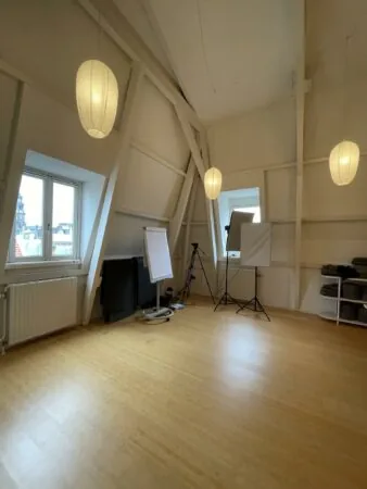 Lichte zolderruimte aan de Raadhuisstraat met houten vloer, flipovers, studiobelichting en opgevouwen yogamatten.