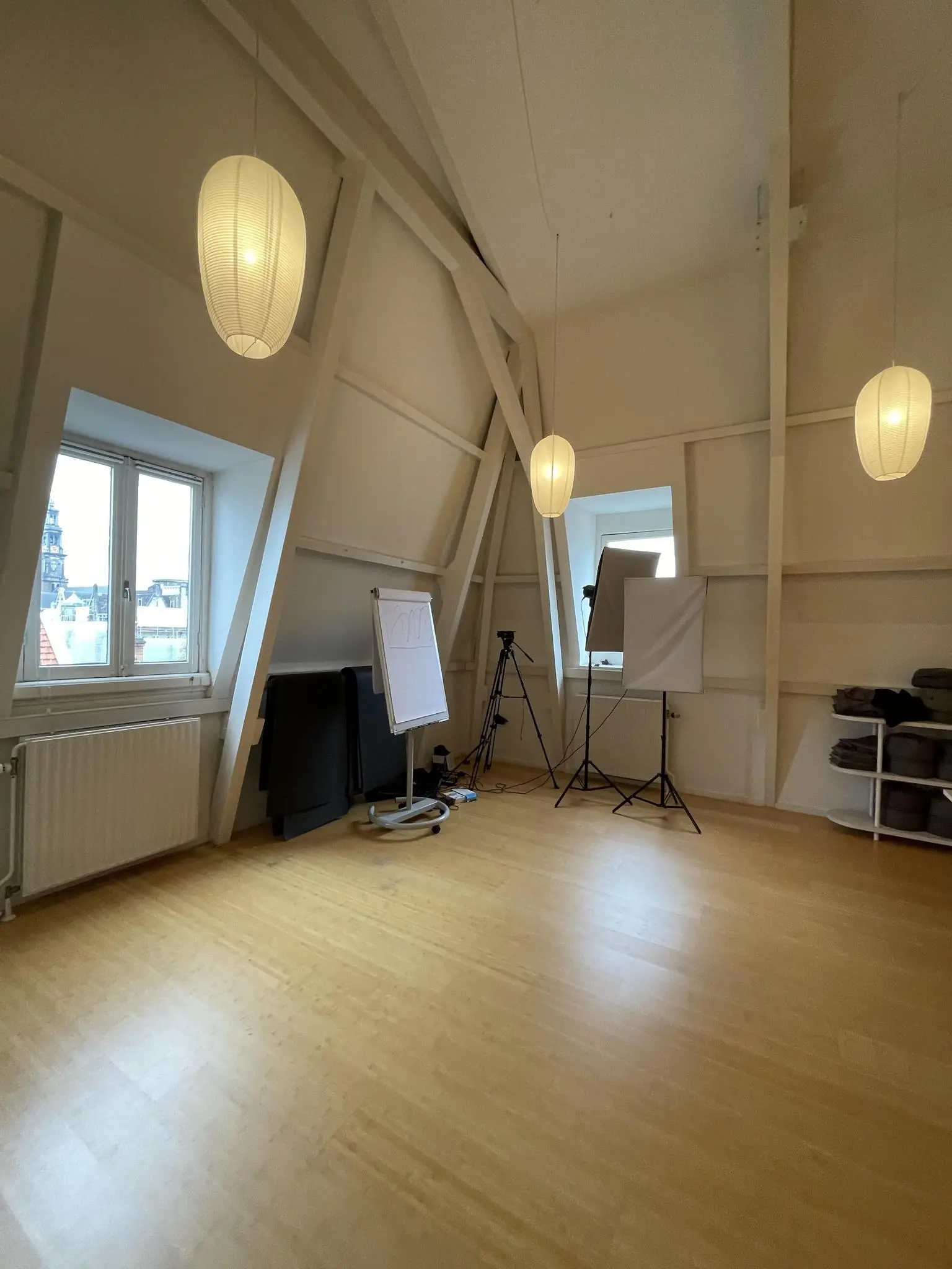Lichte zolderruimte aan de Raadhuisstraat met houten vloer, flipovers, studiobelichting en opgevouwen yogamatten.