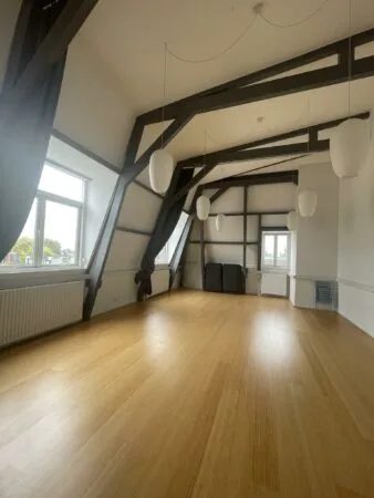 Lichte, ruime zolderkamer aan de Raadhuisstraat met houten vloer, hoge plafonds en hanglampen.
