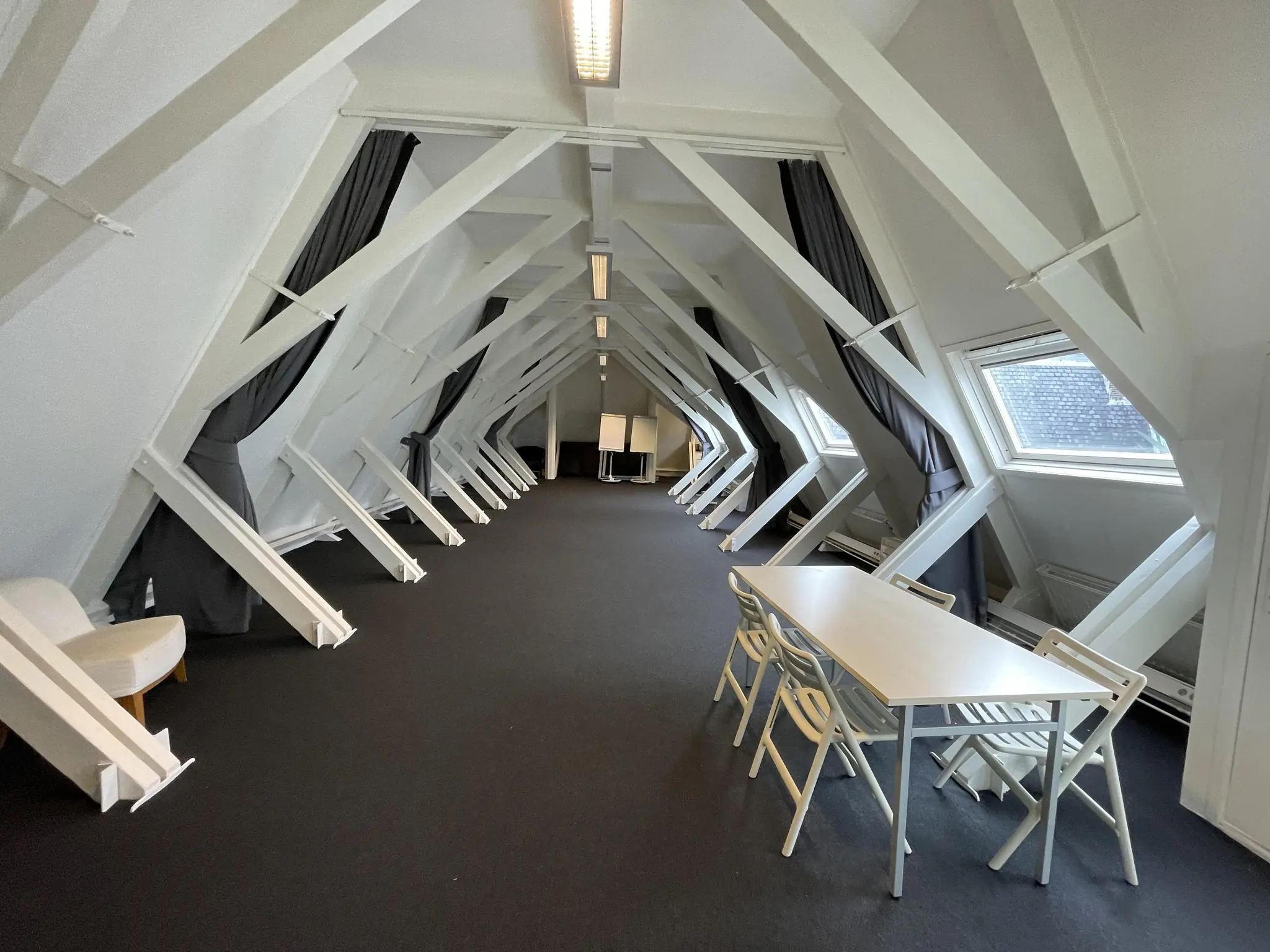 Zolderruimte aan de Raadhuisstraat met witte balkconstructie, tafel, stoelen en dakramen.