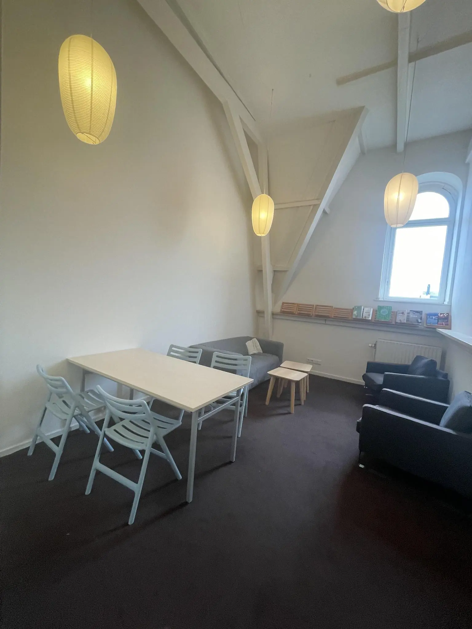 Vergaderruimte aan de Raadhuisstraat met eettafel, zithoek, boekenplank en hanglampen onder een schuin plafond.