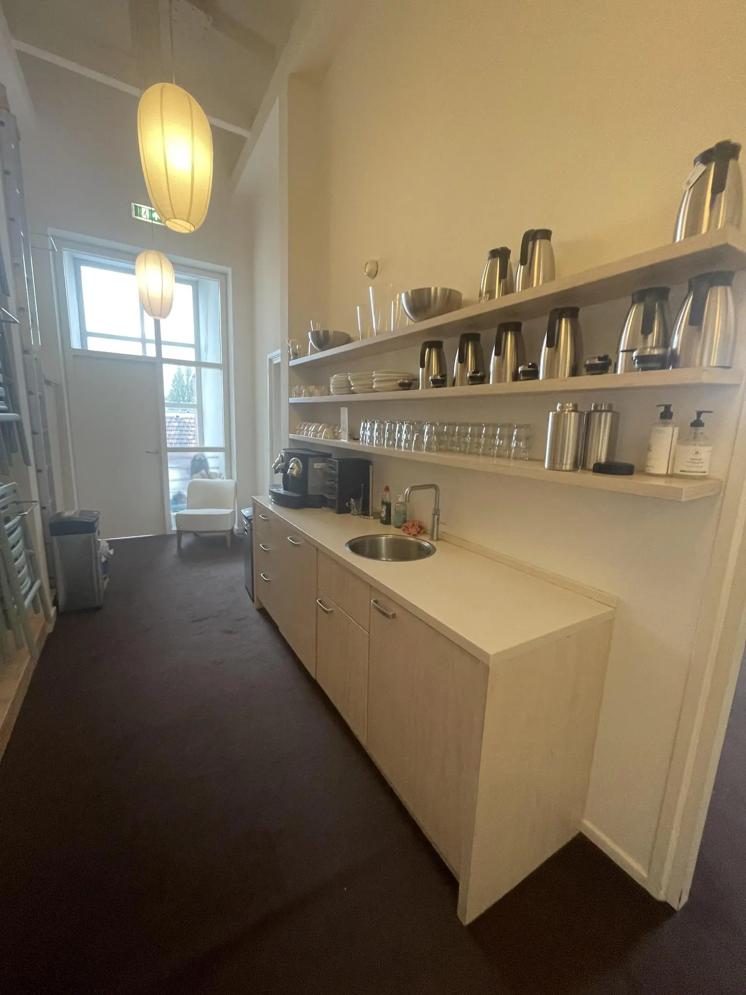 Koffie- en theekeuken met aanrecht, koffiezetapparaat, glazen en thermoskannen in een gang aan de Raadhuisstraat.