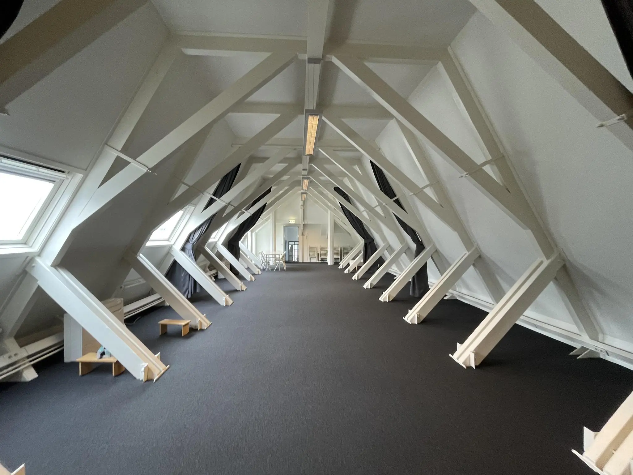 Zolderverdieping van een gebouw aan de Raadhuisstraat met zichtbare dakconstructie, schuine ramen en een donkere vloerbedekking.