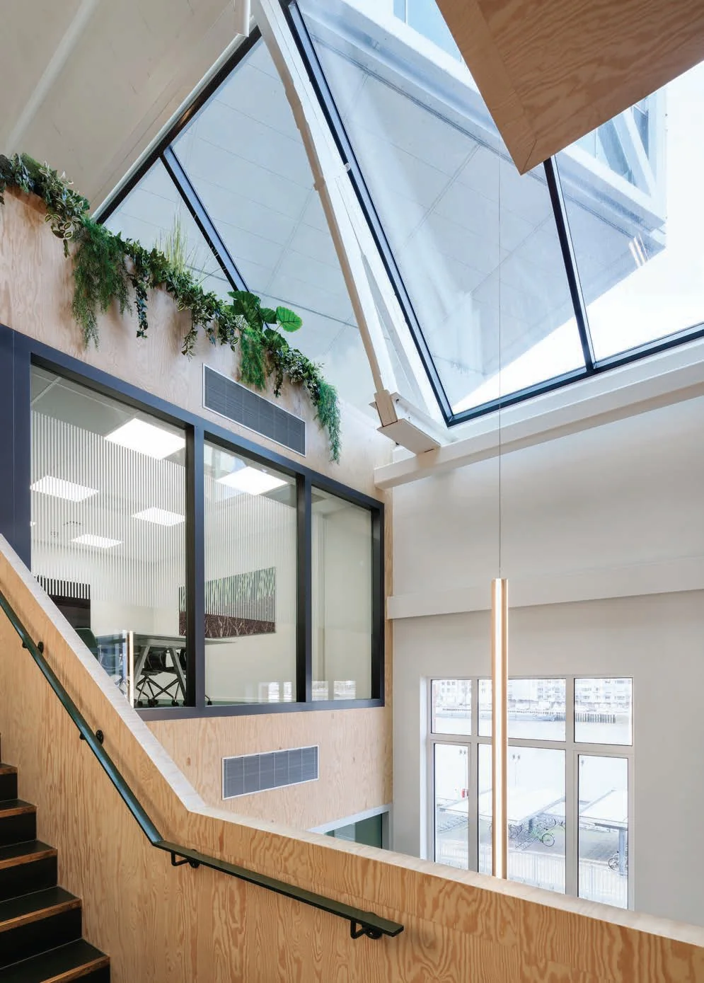 Interieur van een modern kantoorgebouw aan de Nassaukade met houten afwerking, grote ramen en een schuin glazen dak.