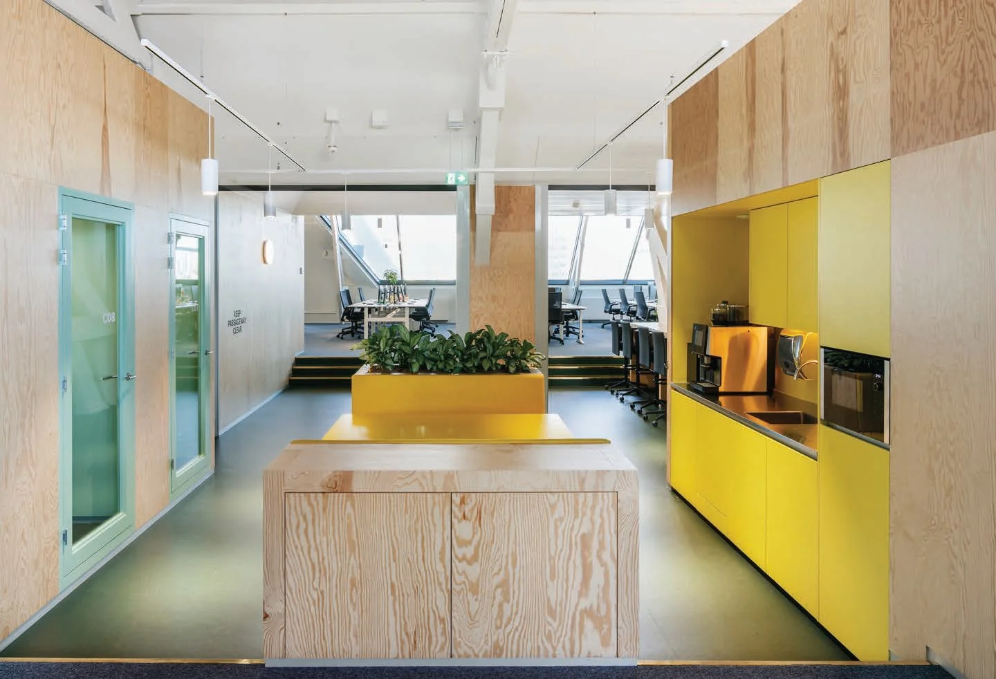 Modern kantoorinterieur aan de Nassaukade met houten wanden, gele accenten, een koffiecorner en werkplekken.