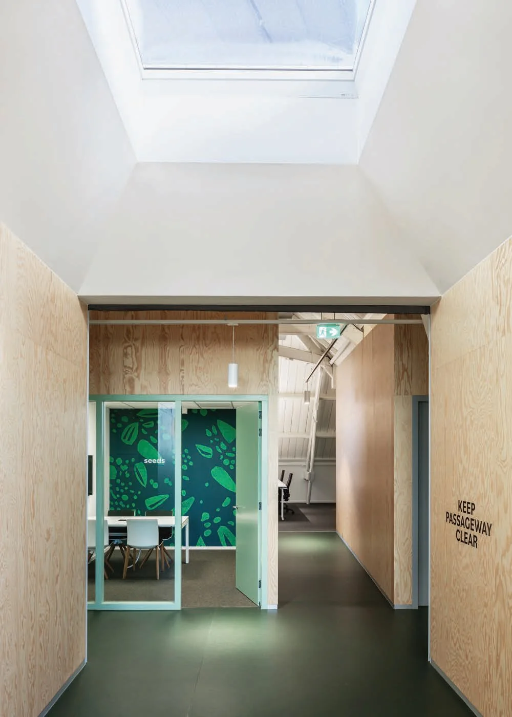 Doorkijk naar een modern kantoorinterieur aan de Nassaukade met houten wanden, glazen vergaderruimte genaamd "seeds" en dakraam voor natuurlijk licht.