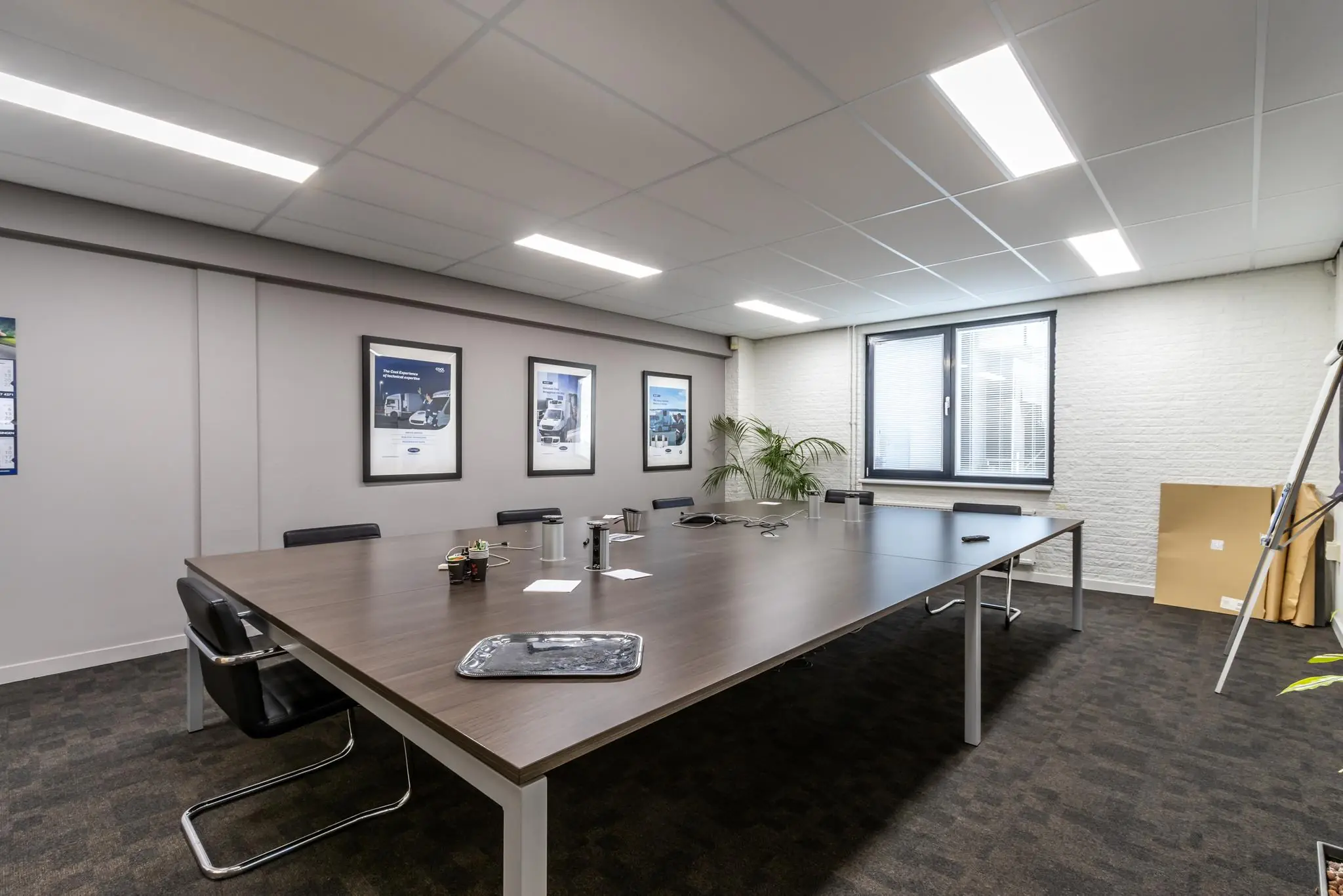 Vergaderruimte met groot rechthoekig tafel, moderne stoelen, posters aan de muur en een raam met jaloezieën aan de Pittsburghstraat.