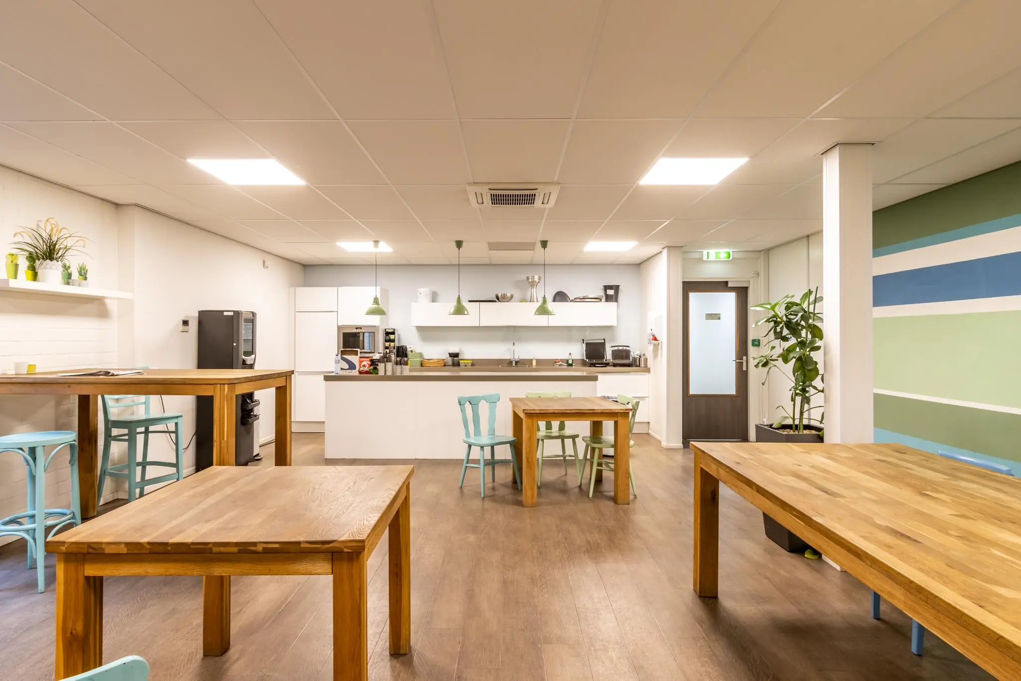 Moderne, netjes ingerichte kantine aan de Pittsburghstraat met houten tafels, pastelkleuren en een open keuken.