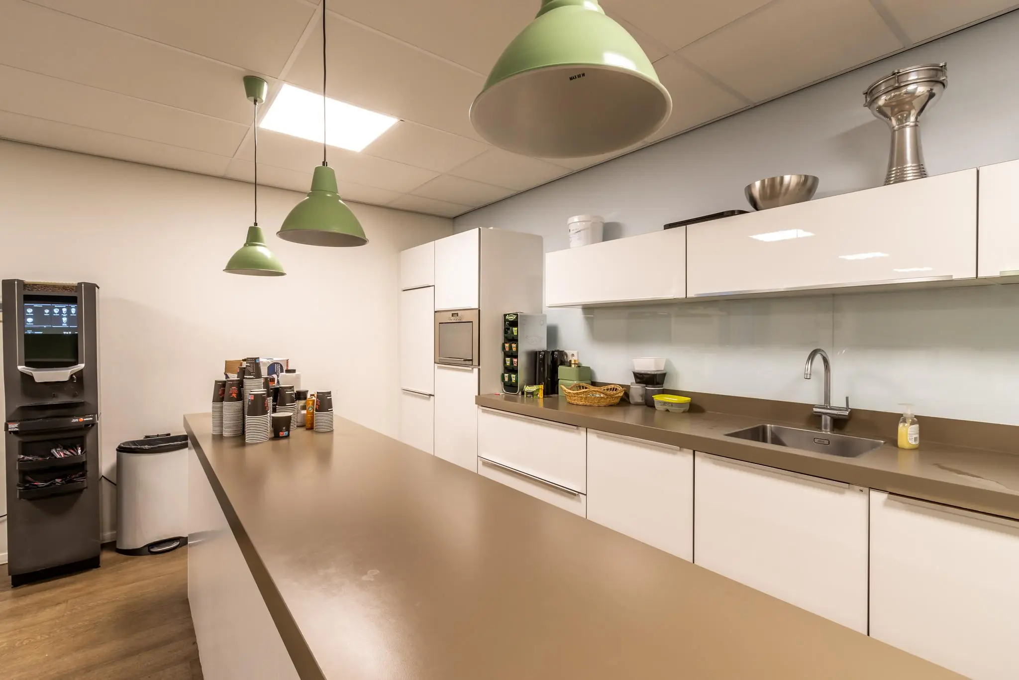 Moderne kantoorkeuken aan de Pittsburghstraat met koffieautomaat, witte kasten en centrale werktafel.