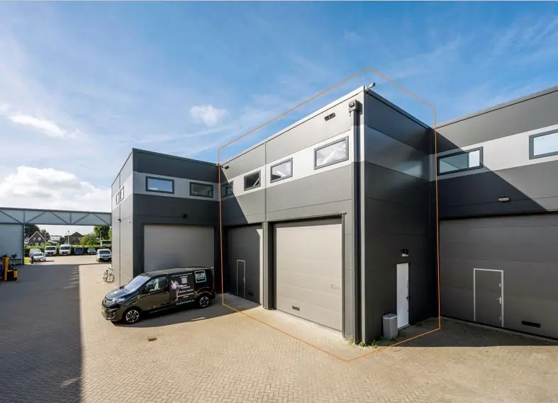 Bedrijfsunit aan de Aalsmeerderweg met grijze gevel, grote roldeur en bovenramen, gelegen op een industrieterrein.