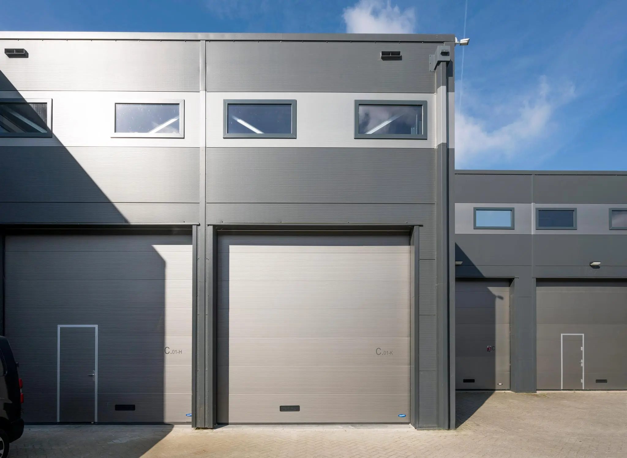 Grijze bedrijfsunits met hoge garagedeuren en bovenramen aan de Aalsmeerderweg, gefotografeerd op een zonnige dag.