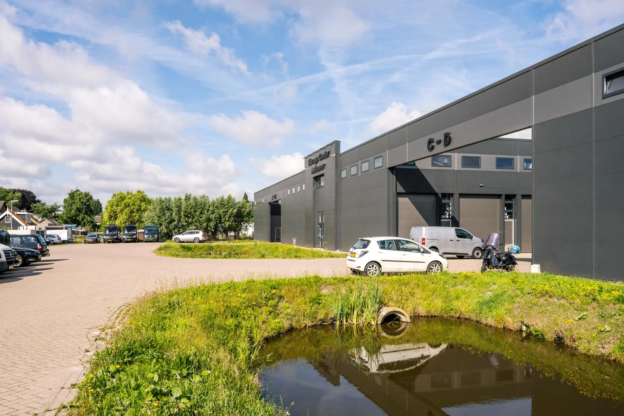 Moderne bedrijfsunits aan de Aalsmeerderweg met parkeerplaatsen en een vijver op de voorgrond.