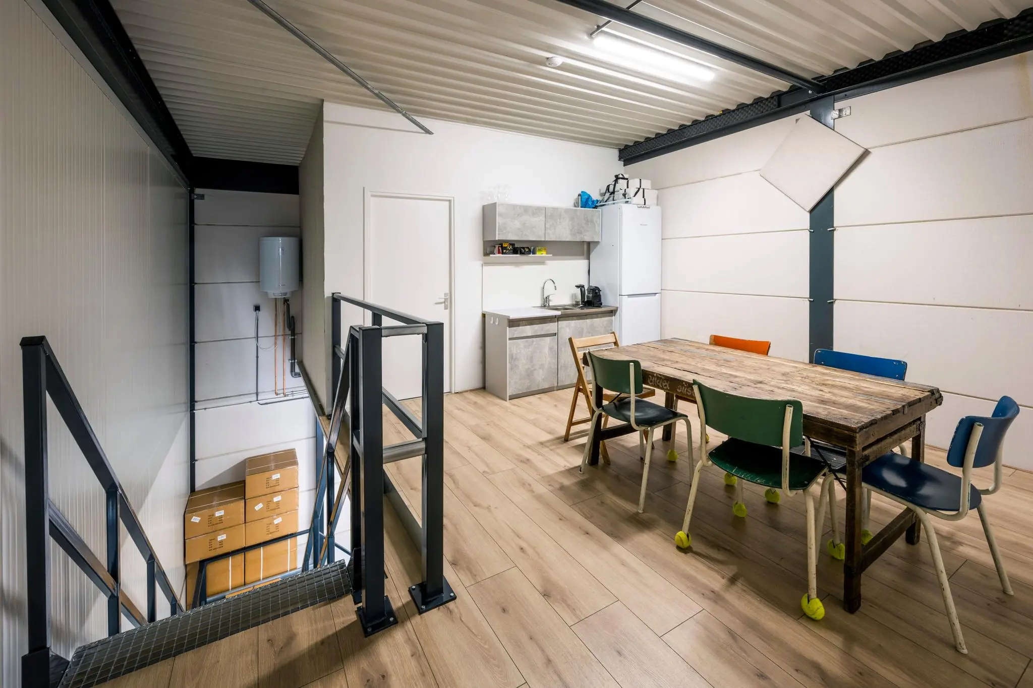 Keukenruimte met houten tafel, kleurrijke stoelen en trap in een bedrijfsruimte aan de Aalsmeerderweg.