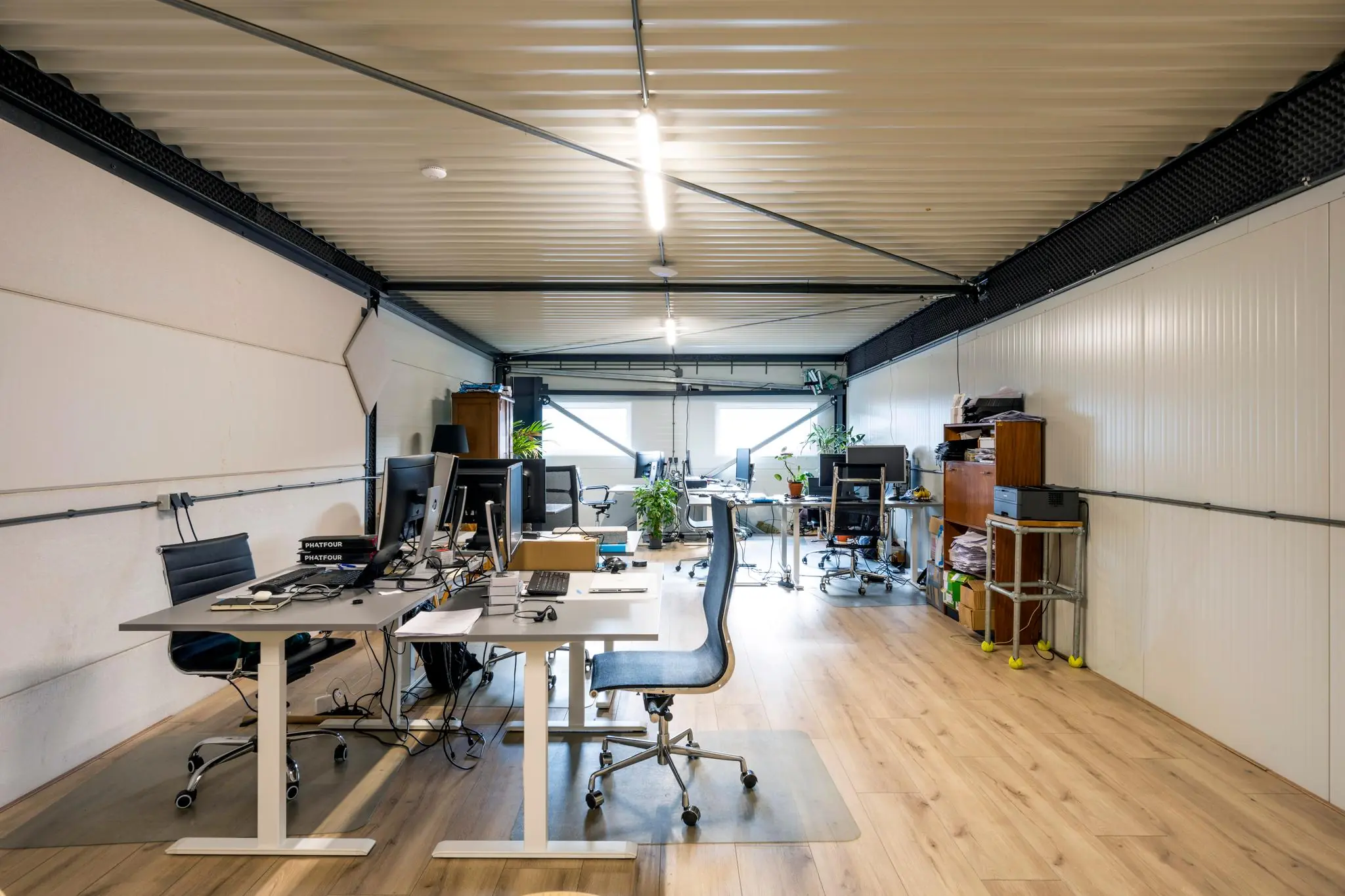 Moderne kantoorruimte aan de Aalsmeerderweg met meerdere bureaus, computers en planten op een houten vloer.