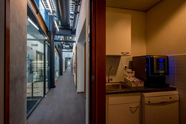 Kantoorgang aan de Fokkerstraat met glazen wanden en een pantry met koffieautomaat.