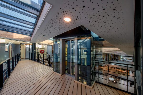 Modern kantoorpand aan de Fokkerstraat met glazen lift en houten loopbrug op de bovenverdieping.