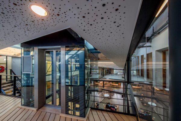 Modern interieur van een kantoorgebouw aan de Fokkerstraat met glazen lift, houten vloeren en zicht op meerdere verdiepingen.