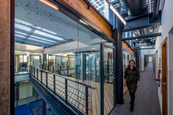 Vrouw loopt door een modern kantoorgebouw aan de Fokkerstraat met glazen wanden en zichtbare houten en stalen constructie.