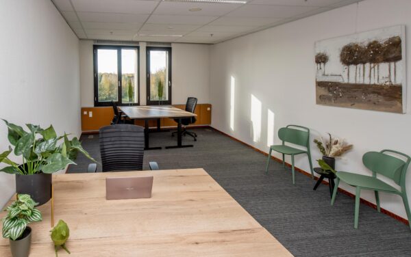 Moderne en lichte kantoorruimte aan de Fokkerstraat met houten bureaus, bureaustoelen, kamerplanten en groen zitgedeelte.