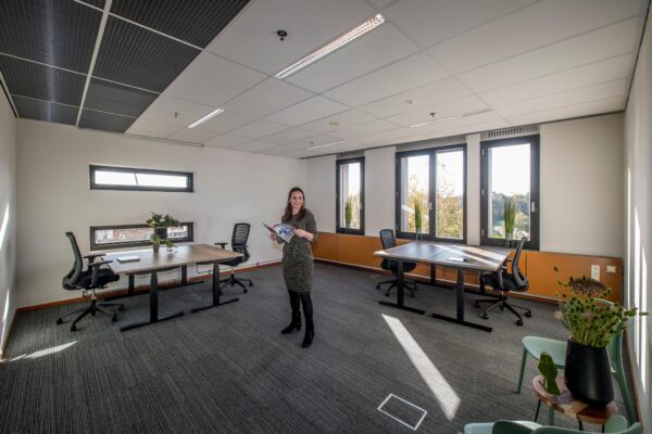 Vrouw staat met een brochure in een modern, licht kantoor aan de Fokkerstraat met meerdere bureaus en bureaustoelen.
