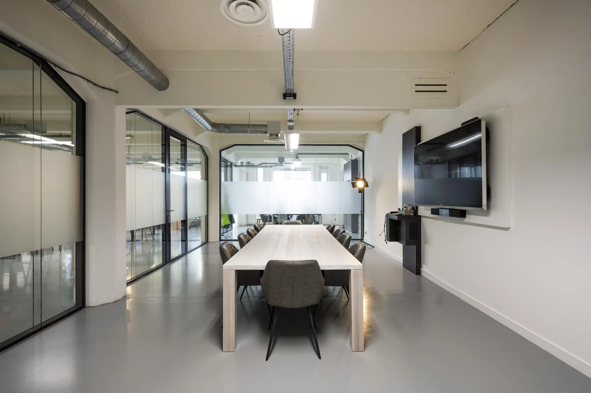 Moderne vergaderruimte aan de Van Diemenstraat met een lange tafel, glazen wanden en een groot presentatiescherm.