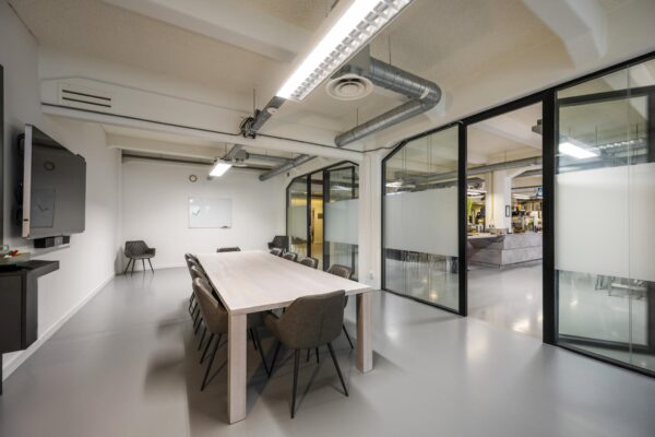 Moderne vergaderruimte aan de Van Diemenstraat met een lange tafel, negen stoelen, glazen wanden en zicht op een open kantoorruimte.