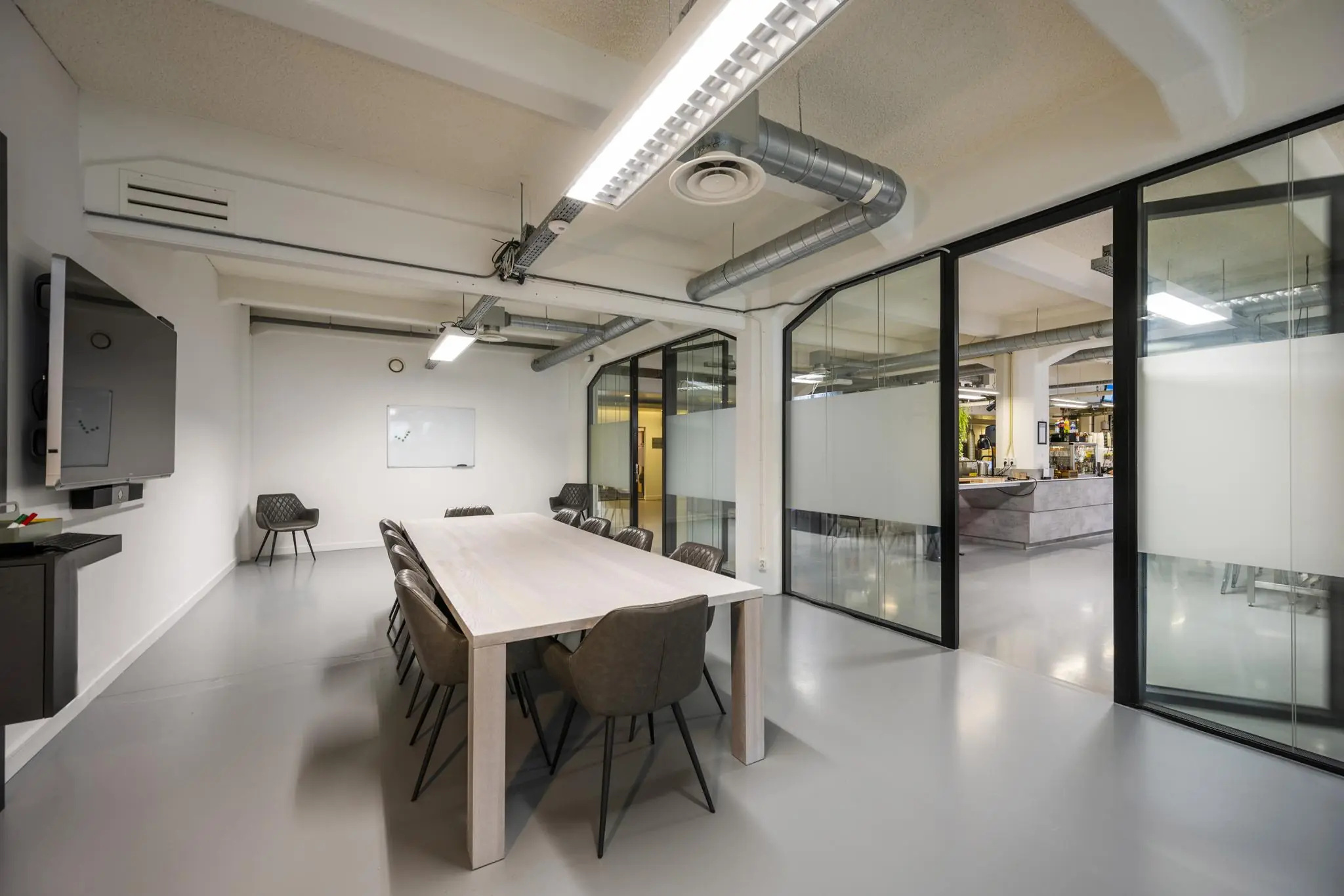 Moderne vergaderruimte aan de Van Diemenstraat met een lange tafel, negen stoelen, glazen wanden en zicht op een open kantoorruimte.