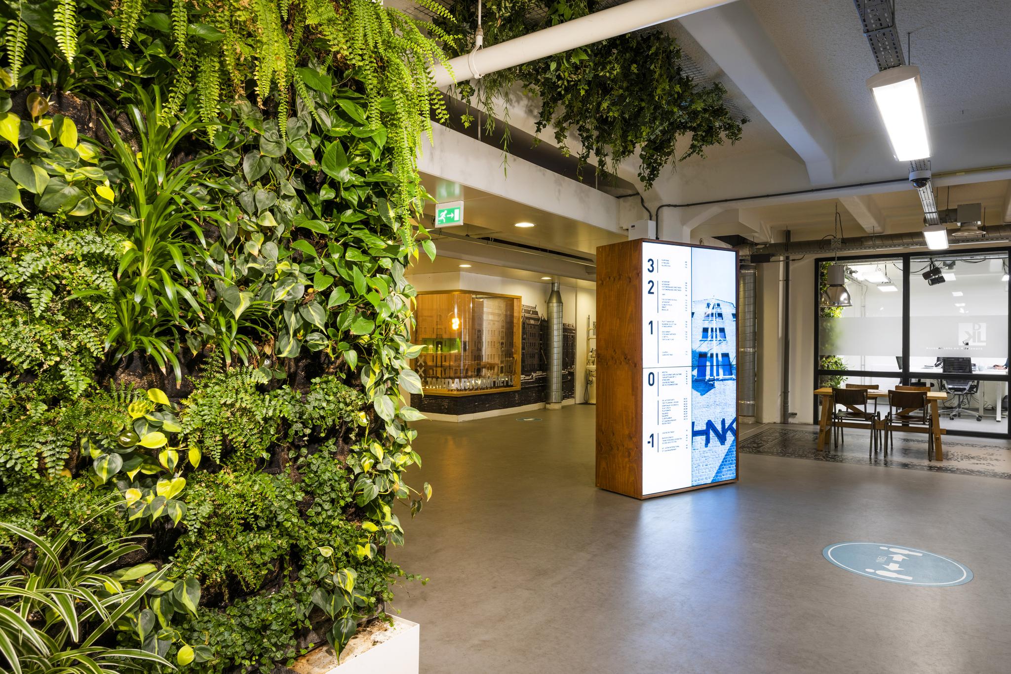 Moderne kantoorentree aan de Van Diemenstraat met een groene plantenmuur, digitale wegwijzer en zicht op vergaderruimtes.