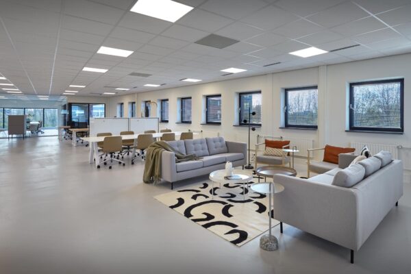 Moderne, open kantoorruimte aan de Joop Geesinkweg met flexwerkplekken en een loungehoek met zitbanken en designmeubilair.