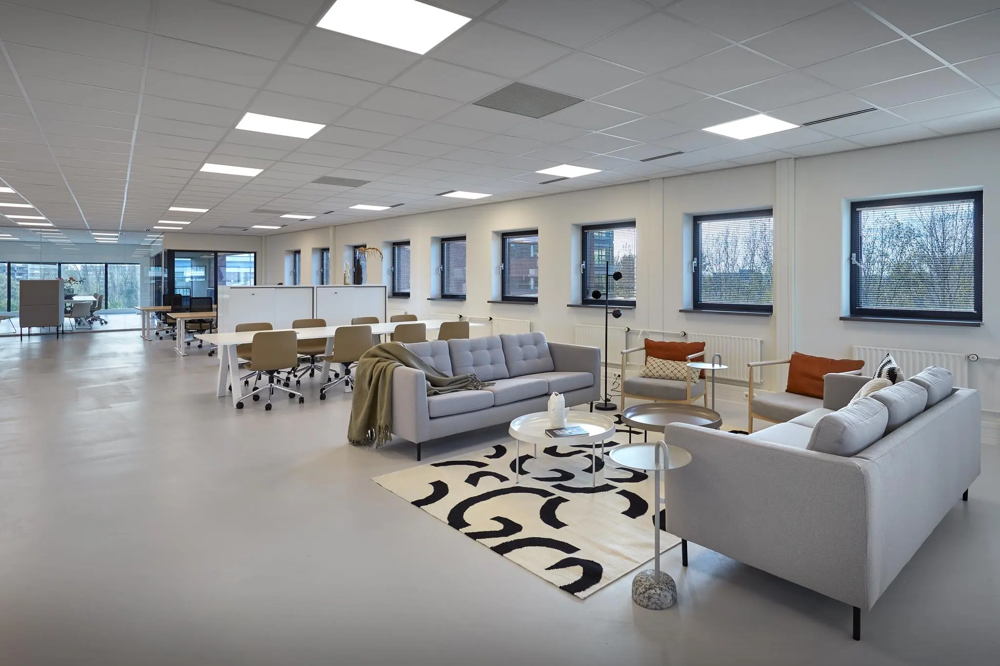 Moderne, open kantoorruimte aan de Joop Geesinkweg met flexwerkplekken en een loungehoek met zitbanken en designmeubilair.