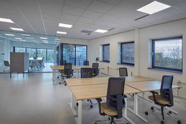 Modern en licht kantoorinterieur aan de Joop Geesinkweg met flexwerkplekken en een glazen vergaderruimte.