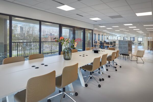 Moderne vergaderruimte aan de Joop Geesinkweg met een lange tafel, beige stoelen en uitzicht op de stad door grote ramen.