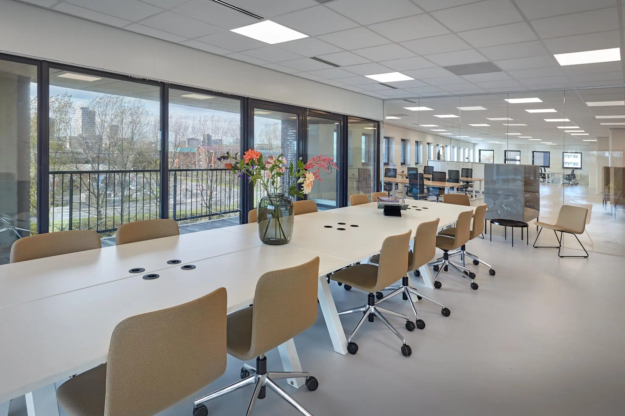 Moderne vergaderruimte aan de Joop Geesinkweg met een lange tafel, beige stoelen en uitzicht op de stad door grote ramen.