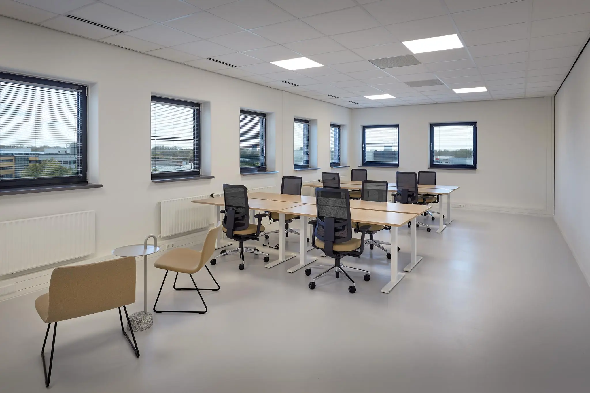 Moderne kantoorruimte aan de Joop Geesinkweg met bureaus, bureaustoelen en grote ramen met zonwering.