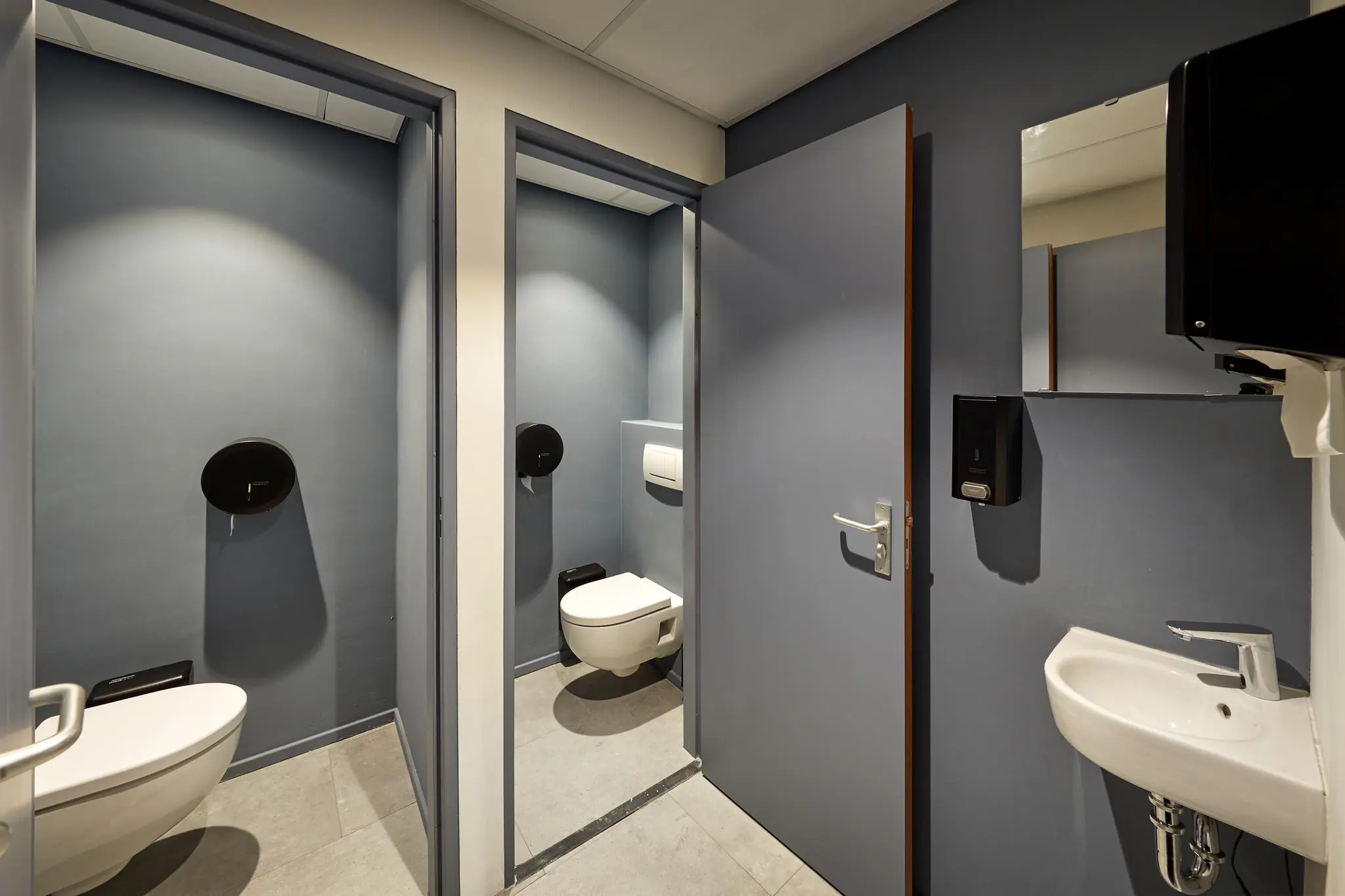 Moderne toiletruimte aan de Joop Geesinkweg met twee afgesloten wc-hokjes en een wasbak met spiegel.