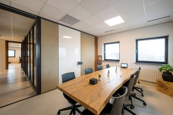 Vergaderruimte aan de Joop Geesinkweg met een robuuste houten tafel, moderne stoelen en natuurlijk licht via twee ramen.