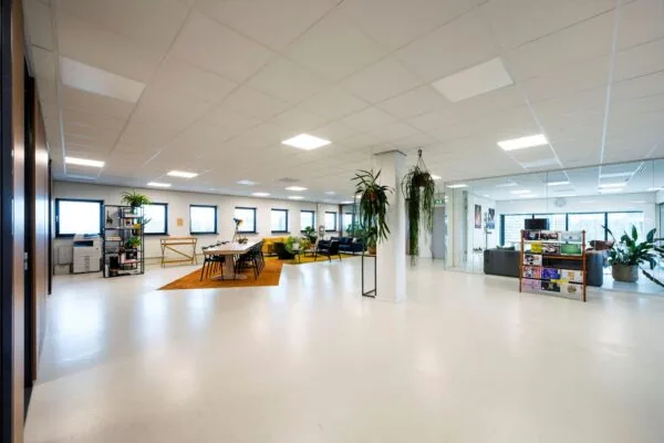 Moderne en ruime kantoorruimte aan de Joop Geesinkweg met vergadertafel, zithoeken, planten en glazen wanden.