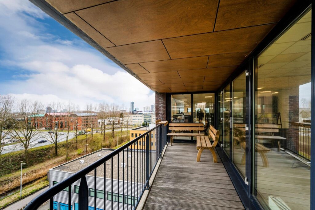 Houten balkon met zitbanken aan de Joop Geesinkweg, uitkijkend over kantoren en snelweg in Amsterdam.