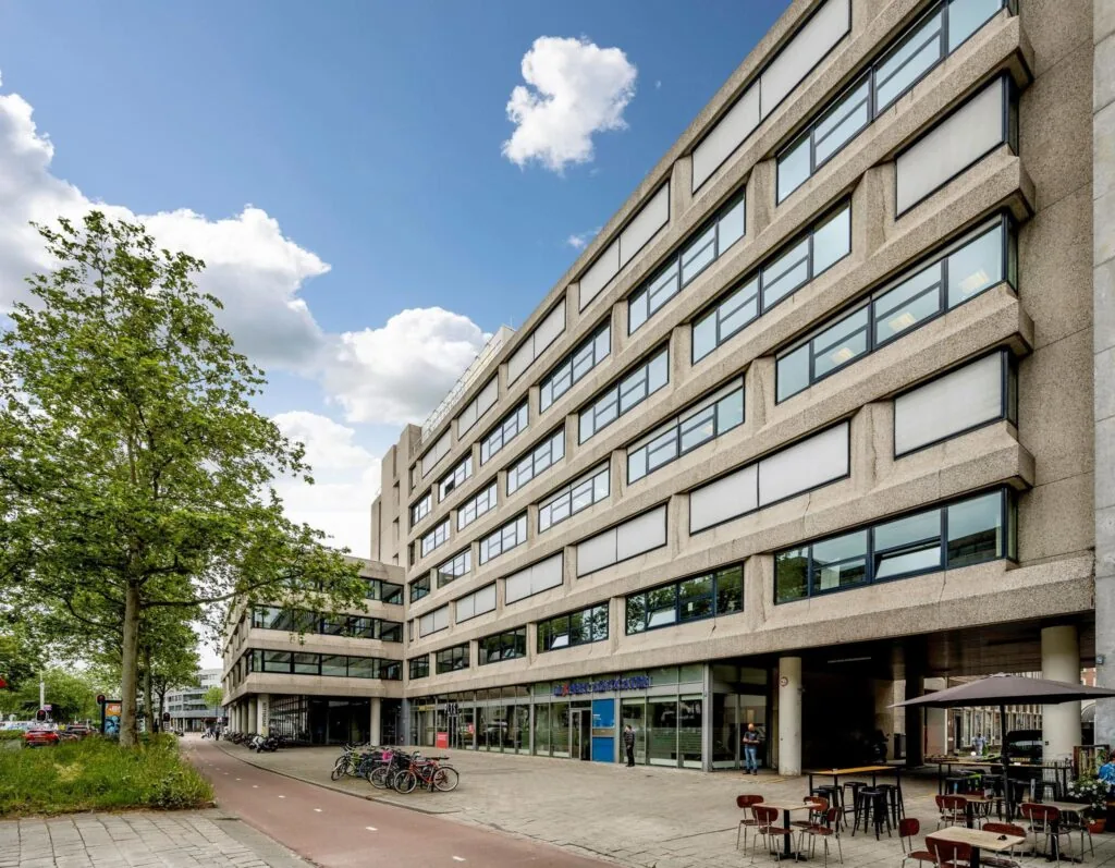 Kantoorgebouw aan de Westblaak in Rotterdam met fietsen, terras en blauwe lucht op de achtergrond.