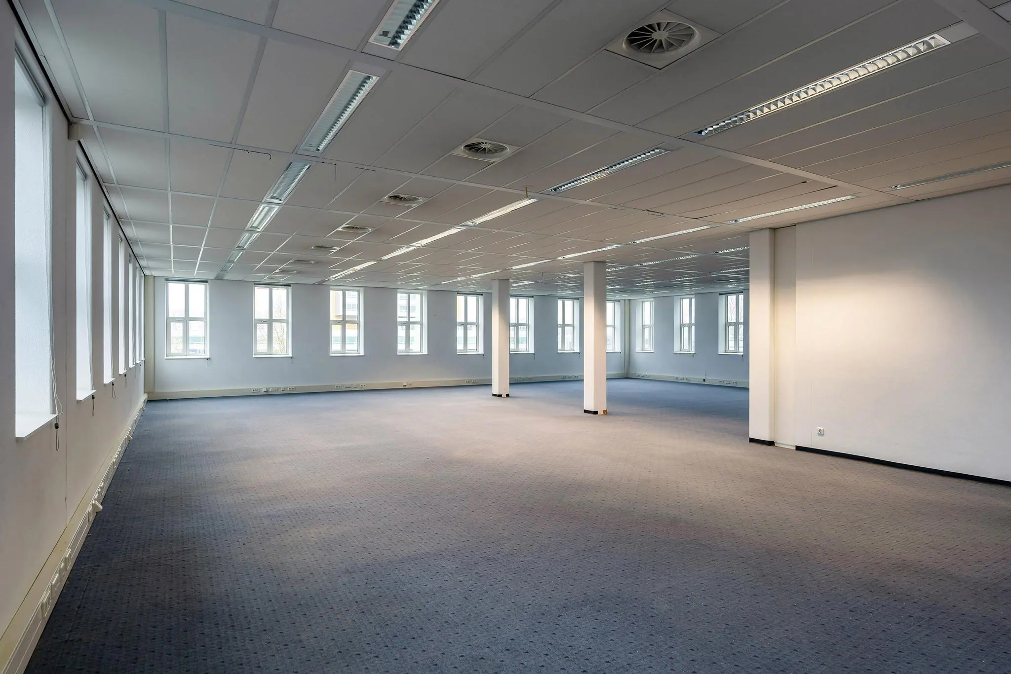 Leeg kantoorruimte aan de Vareseweg met systeemplafond, pilaren en meerdere ramen.